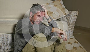 Lifestyle portrait young attractive sad and depressed man sitting on living room floor feeling desperate and stressed suffering