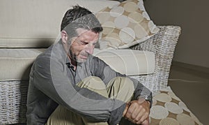 Lifestyle portrait young attractive sad and depressed man sitting on living room floor feeling desperate and stressed suffering