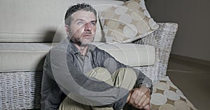 Lifestyle portrait young attractive sad and depressed man sitting on living room floor feeling desperate and stressed suffering