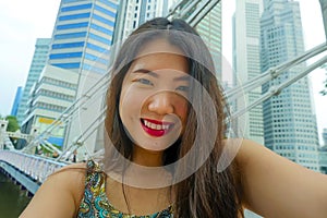 Lifestyle portrait of young beautiful and happy Asian Chinese tourist woman taking selfie photo with mobile phone smiling cheerful