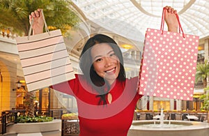 Lifestyle portrait of young beautiful and happy Asian Chinese woman holding shopping bags at modern shopping mall smiling excited