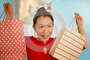 Lifestyle portrait of young beautiful and happy Asian Chinese woman holding shopping bags at modern shopping mall smiling excited