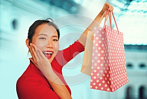 Lifestyle portrait of young beautiful and happy Asian Chinese woman holding shopping bags at modern shopping mall smiling excited