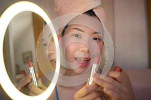 Lifestyle portrait of young beautiful and happy Asian woman applying makeup and beauty facial treatment looking in mirror at home