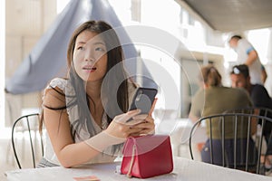 Lifestyle portrait of young beautiful and sweet Asian Chinese woman sitting happy outdoors at street cafe using internet travel