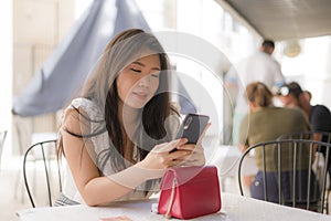 Lifestyle portrait of young beautiful and sweet Asian Japanese woman sitting happy outdoors at street cafe using internet travel