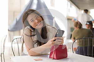 Lifestyle portrait of young beautiful and sweet Asian Korean woman sitting happy outdoors at street cafe using internet travel and