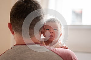 Lifestyle portrait of young father holding adorable and beautiful newborn baby girl looking towards camera portraying sweet