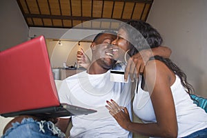 Lifestyle portrait of young happy and attractive black African American couple enjoying at home using credit card and laptop