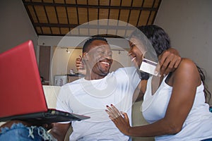 Lifestyle portrait of young happy and attractive black afro American couple enjoying at home using credit card and laptop computer