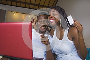 Lifestyle portrait of young happy and attractive black afro American couple enjoying at home using credit card and laptop computer