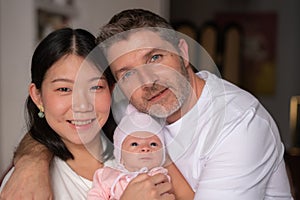 Lifestyle portrait of young happy and attractive mixed ethnicity couple holding newborn baby girl smiling cheerful in parenting