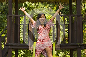 Lifestyle portrait of young happy and beautiful Asian Chinese woman in sweet Summer dress playing on slide at city park smiling