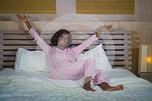 Lifestyle portrait of young happy and beautiful black afro American woman in pajamas lying relaxed and playful on bed smiling