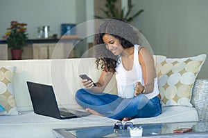 Lifestyle portrait of young happy and beautiful black afro American woman using internet texting on mobile phone while working on