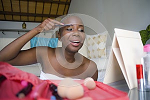 Lifestyle portrait of young happy and beautiful black afro American woman wrapped in towel applying face makeup eyebrow profiling