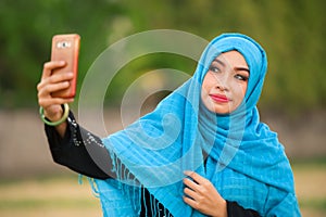 Lifestyle portrait of young happy and beautiful tourist woman in muslim hijab head scarf taking selfie picture with mobile phone p