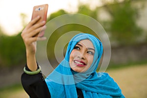 Lifestyle portrait of young happy and beautiful tourist woman in muslim hijab head scarf taking selfie picture with mobile phone p
