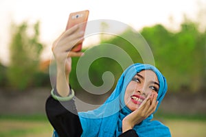 Lifestyle portrait of young happy and beautiful tourist woman in muslim hijab head scarf taking selfie picture with mobile phone p