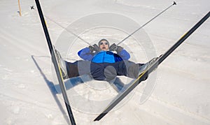 Lifestyle portrait of young happy and funny man in cross country ski lying on snow playful enjoying winter holidays on Swiss Alps