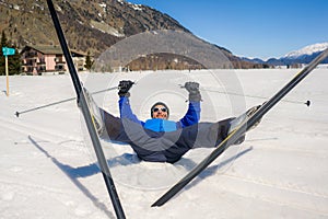 Lifestyle portrait of young happy and funny man in cross country ski lying on snow playful enjoying winter holidays on Swiss Alps