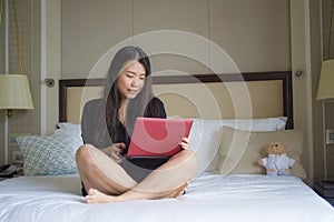 Lifestyle portrait of young happy and relaxed Asian Korean woman at hotel room bed working with laptop computer cheerful in busine