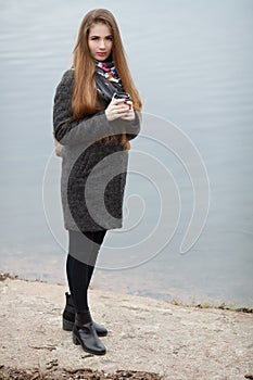 Lifestyle portrait of young and pretty adult woman with gorgeous long hair posing with coffee cup near water in city park