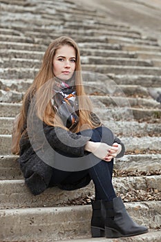 Lifestyle portrait of young and pretty adult woman with gorgeous long hair posing sitting on concrete stairway looking into camera