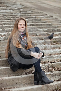 Lifestyle portrait of young and pretty adult woman with gorgeous long hair posing sitting on concrete stairway looking into camera