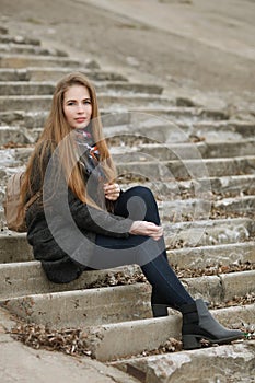 Lifestyle portrait of young and pretty adult woman with gorgeous long hair posing sitting on concrete stairway looking into camera