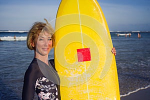 Young beautiful and happy surfer girl holding yellow surf board smiling cheerful enjoying summer holidays in tropical beach w