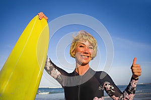 Young beautiful and happy surfer woman holding yellow surf board smiling cheerful enjoying summer holidays in tropical beach