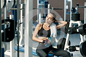 Lifestyle portrait of a young sporty woman drinking water from blue bottle in a fitness studio