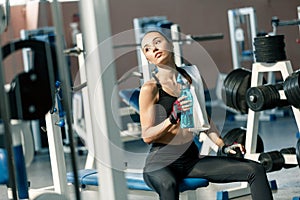 Lifestyle portrait of a young sporty woman drinking water from blue bottle in a fitness studio