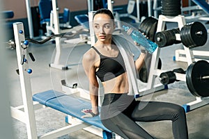 Lifestyle portrait of a young sporty woman drinking water from blue bottle in a fitness studio