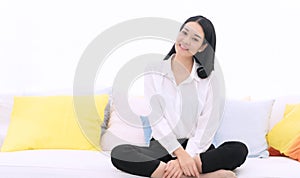 Lifestyle relaxation concept. Cheerful young woman sitting on white couch with pillow in living room at home