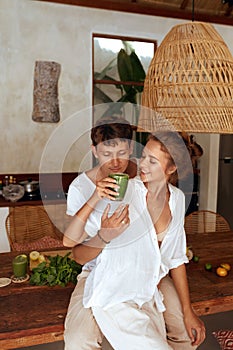 Lifestyle. Romantic Couple At Kitchen Hugging And Drinking Smoothie. Woman Holding Glass Of Detox Cocktail.