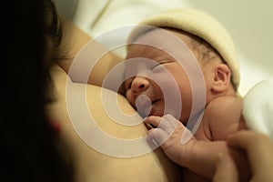 Lifestyle shot of woman holding adorable newborn baby girl skin on skin  immediately after birth laying happy on hospital bed in