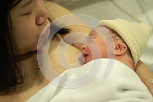 Lifestyle shot of woman holding adorable newborn baby girl skin on skin  immediately after birth laying happy on hospital bed in