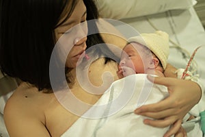 Lifestyle shot of woman holding adorable newborn baby girl skin on skin  immediately after birth laying happy on hospital bed in