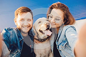 Lifestyle summer walk concept. Happy couple making selfie photo with new pet dog retriever Labrador outdoors