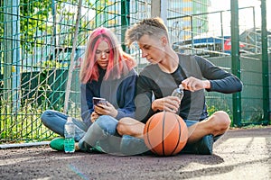 Lifestyle teenagers, boy and girl on basketball court sitting with ball