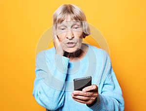 Lifestyle, tehnology and people concept: old granny looks at her phone and is surprised