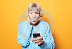 Lifestyle, tehnology  and people concept: old granny looks at her phone and is surprised