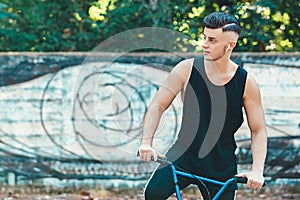 Lifestyle, transport and people concept - young man with bluetooth headphones posing on bicycle on city street