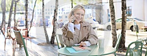 Lifestyle and urban people concept. Young smiling girl, student sitting in cafe outdoors, talking on mobile phone