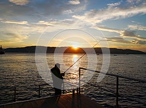 Lifestyle and vacation concept. At sunset, a man is fishing on the pier. Selective focus and copyspace