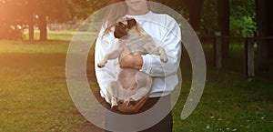 Lifestyle woman holding pug dog and smiling. Loving dog in his owner`s arms in the park. Concept of caring for a pet and animal