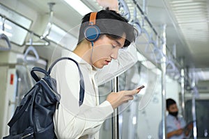 A lifestyle of young Asian man using cellphone with headset while taking the subway train to work at the rush hour morning