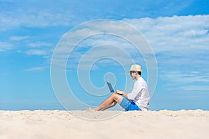 Lifestyle young asian man working on laptop while sitting chill on the beautiful beach, freelance working social on holiday summer